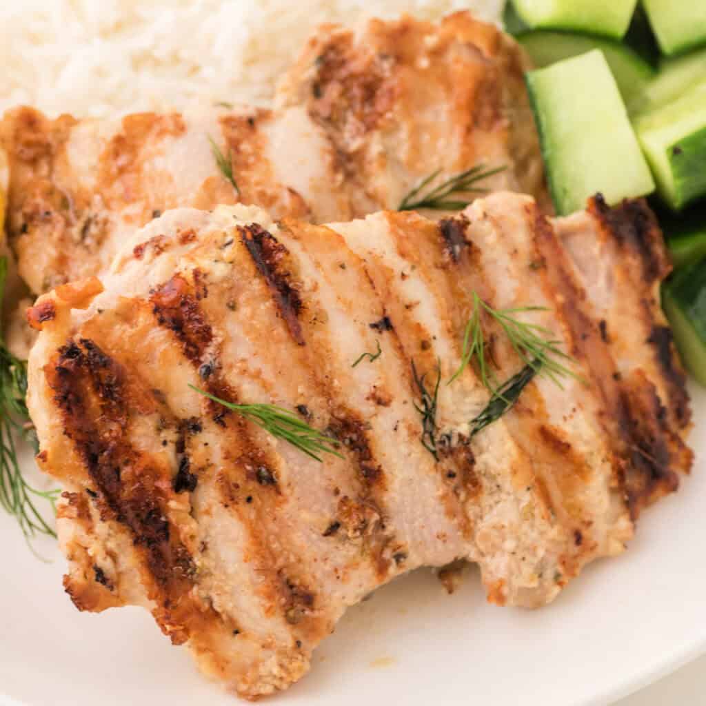 Square crop of grilled tahini chicken with visible grill marks and fresh dill garnish.