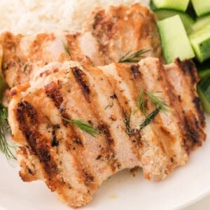 Square crop of grilled tahini chicken with visible grill marks and fresh dill garnish.