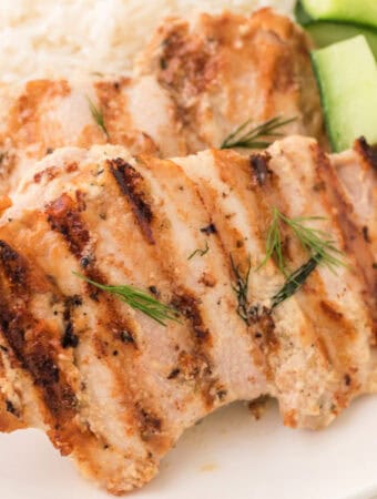 Square crop of grilled tahini chicken with visible grill marks and fresh dill garnish.