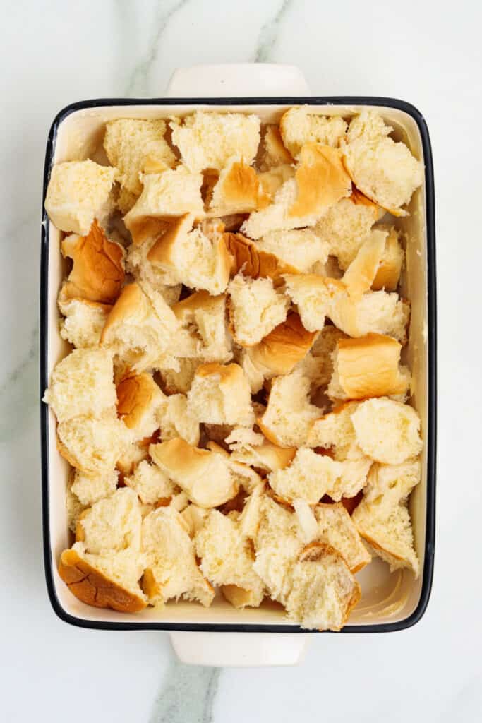 Torn Hawaiian rolls arranged in a greased rectangular baking dish ready for custard mixture
