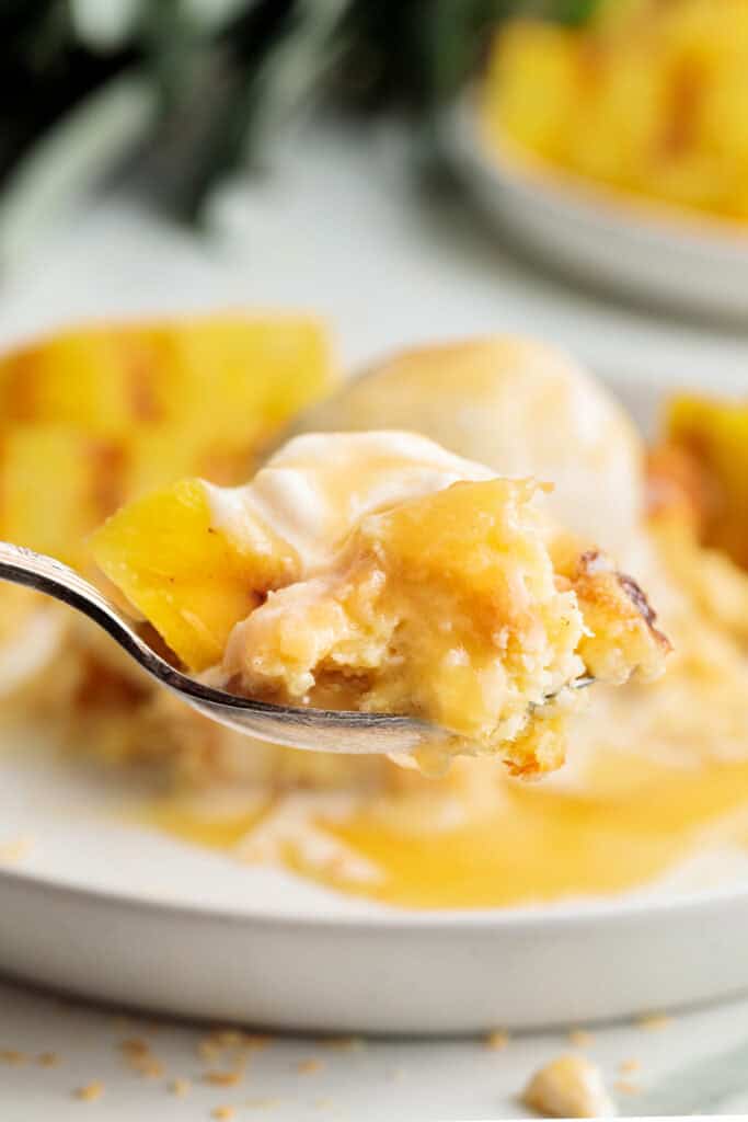 Fork holding a bite of Piña Colada Bread Pudding with melted ice cream and pineapple pieces
