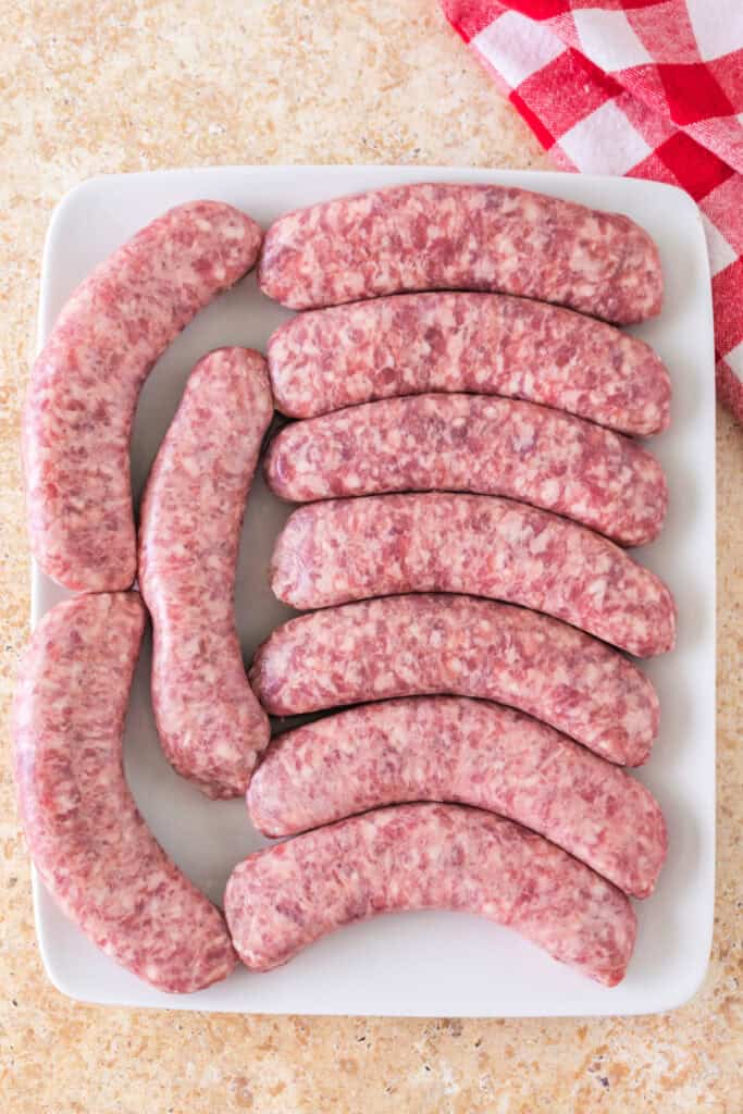 Raw bratwurst sausages neatly arranged on a white plate, ready for smoking.