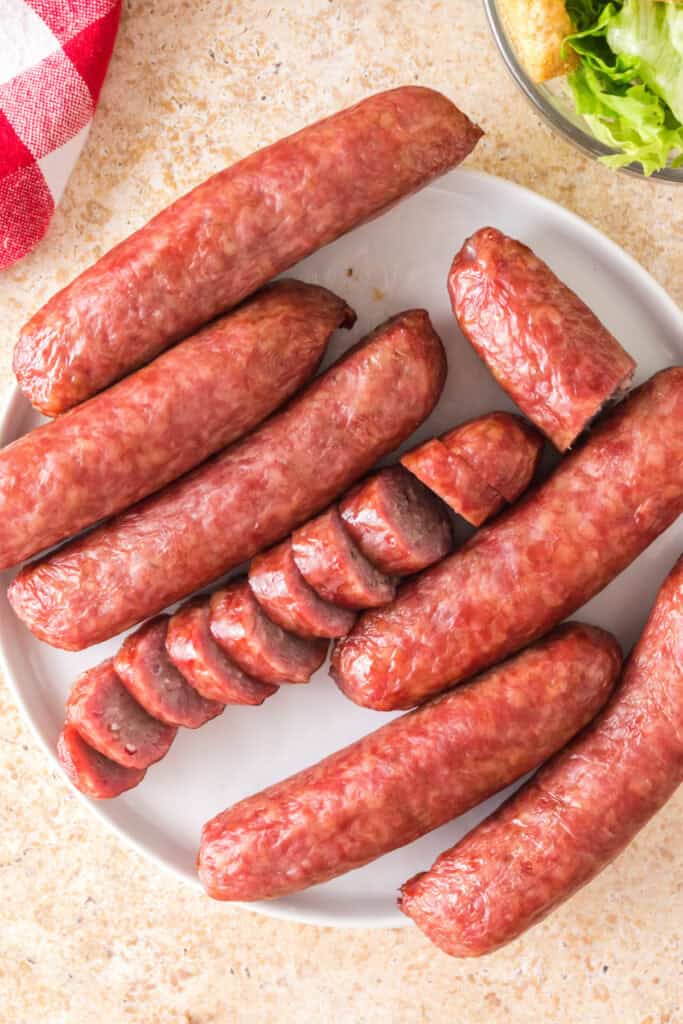 Fully smoked bratwursts sliced and whole, served on a plate with salad nearby.