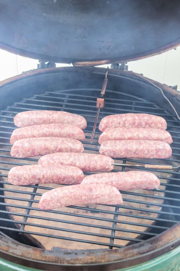 Bratwursts placed on the grill inside a smoker with visible smoke rising.