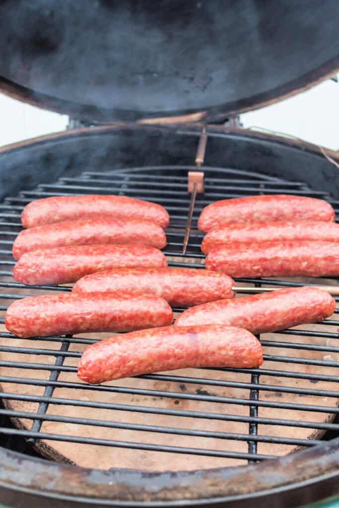 Bratwursts starting to brown as they smoke on the grill inside a smoker.