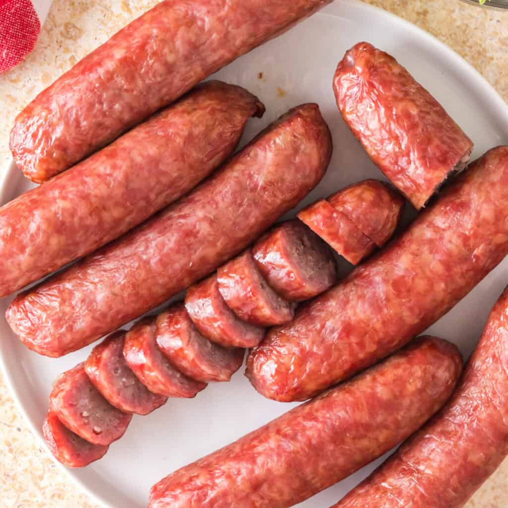 Overhead view of whole and sliced smoked bratwursts arranged on a white plate.