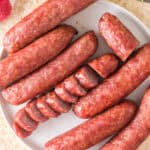 Overhead view of whole and sliced smoked bratwursts arranged on a white plate.