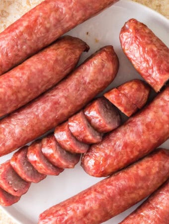 Overhead view of whole and sliced smoked bratwursts arranged on a white plate.