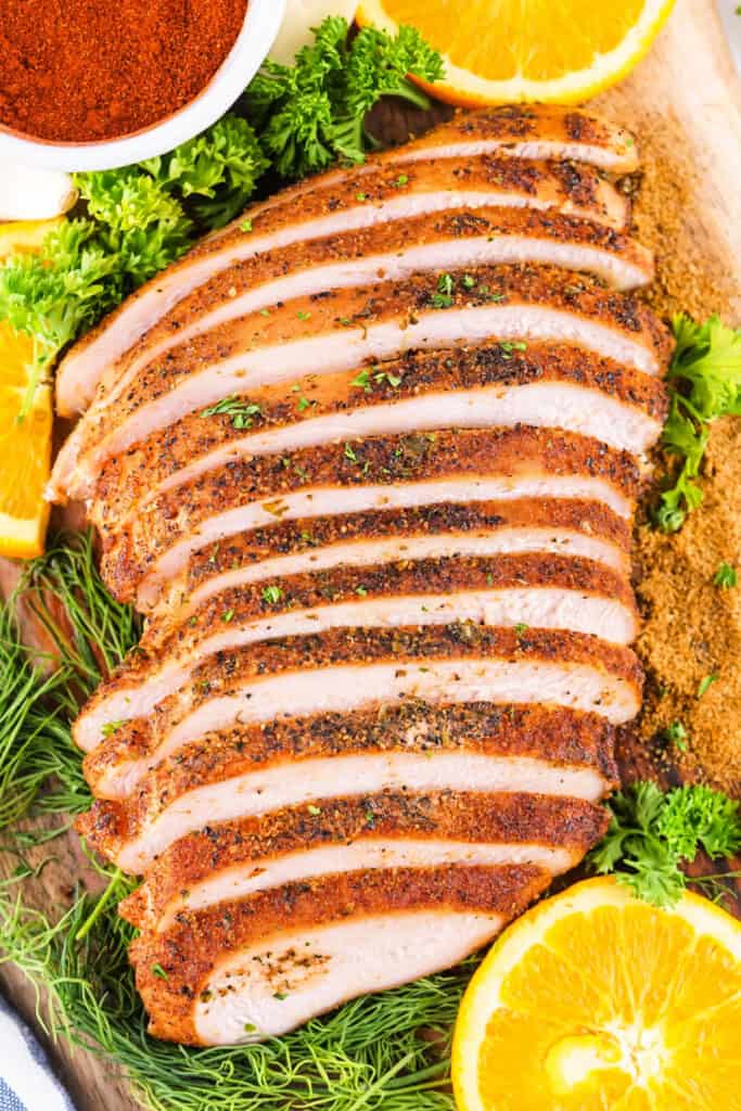 Sliced smoked Cajun turkey breast arranged on a cutting board with fresh herbs and orange slices