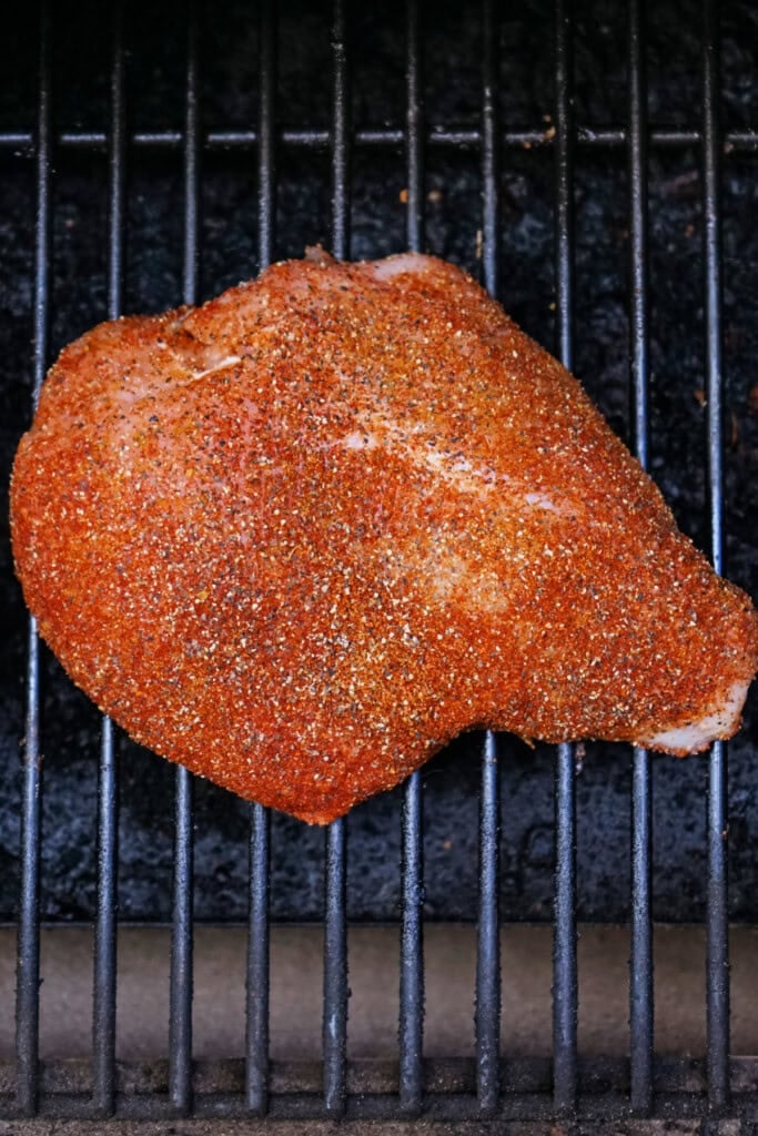 Raw seasoned Cajun turkey breast sitting on the smoker grate ready to cook