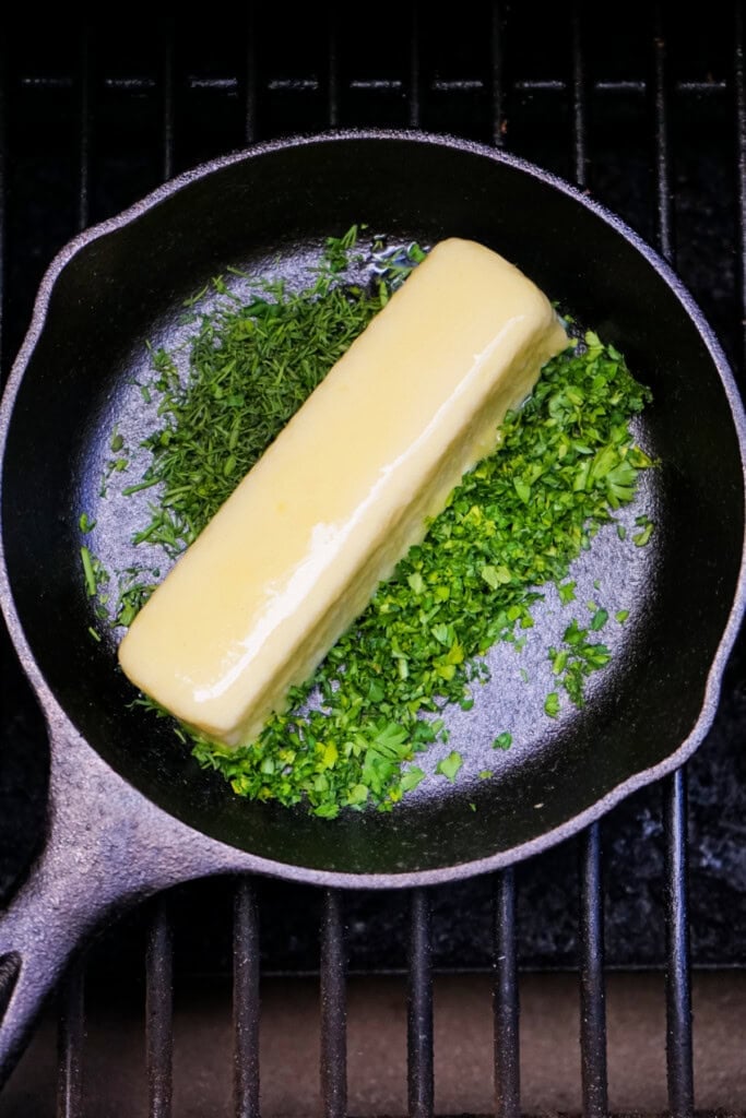 Stick of butter with fresh chopped dill and parsley in a small cast iron skillet on the smoker