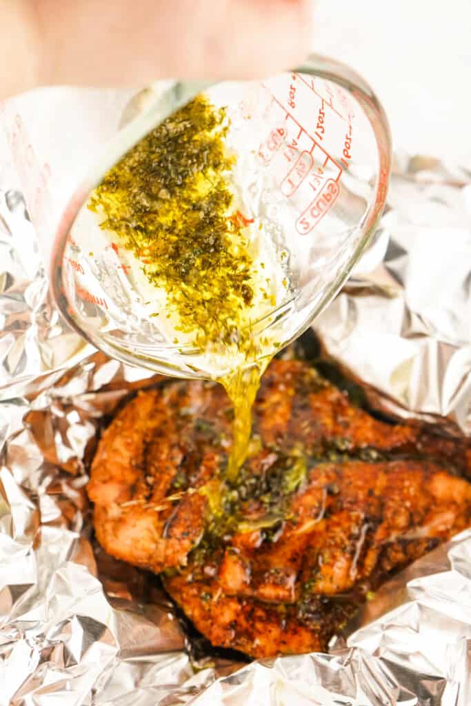 Pouring melted herb butter mixture from a measuring cup over smoked Cajun turkey in foil