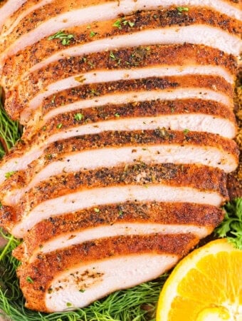 Square image of sliced smoked Cajun turkey breast surrounded by fresh herbs, seasoning, and orange slices