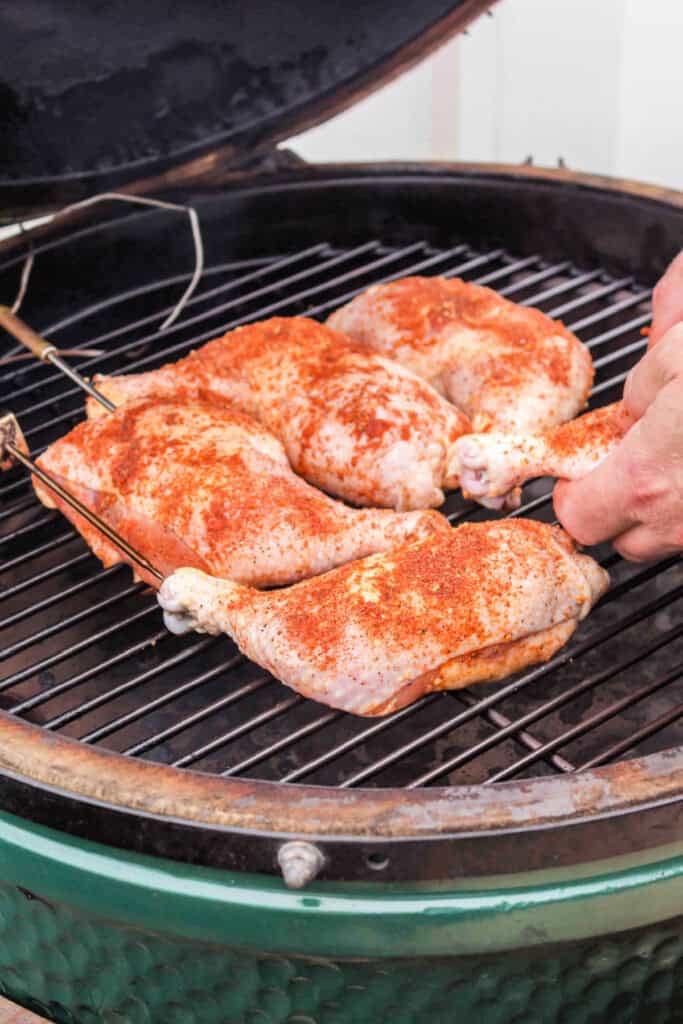 Raw seasoned chicken quarters being placed on a smoker grill