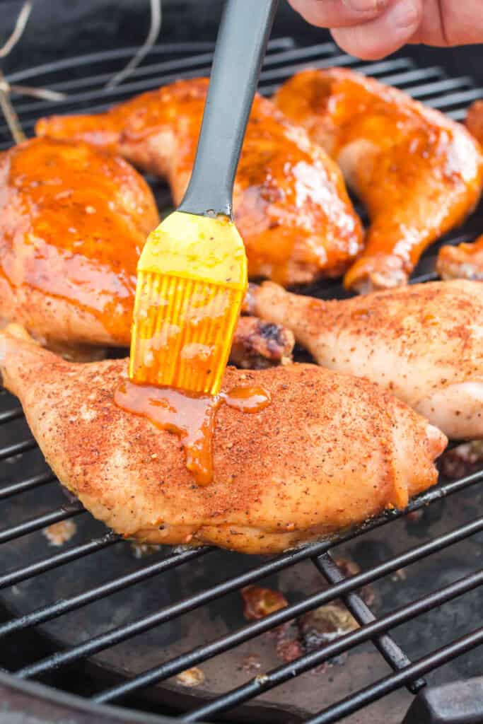 Chicken quarters on smoker grill being glazed with BBQ sauce