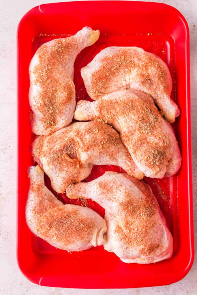 Chicken quarters in a red tray coated with dry rub seasoning