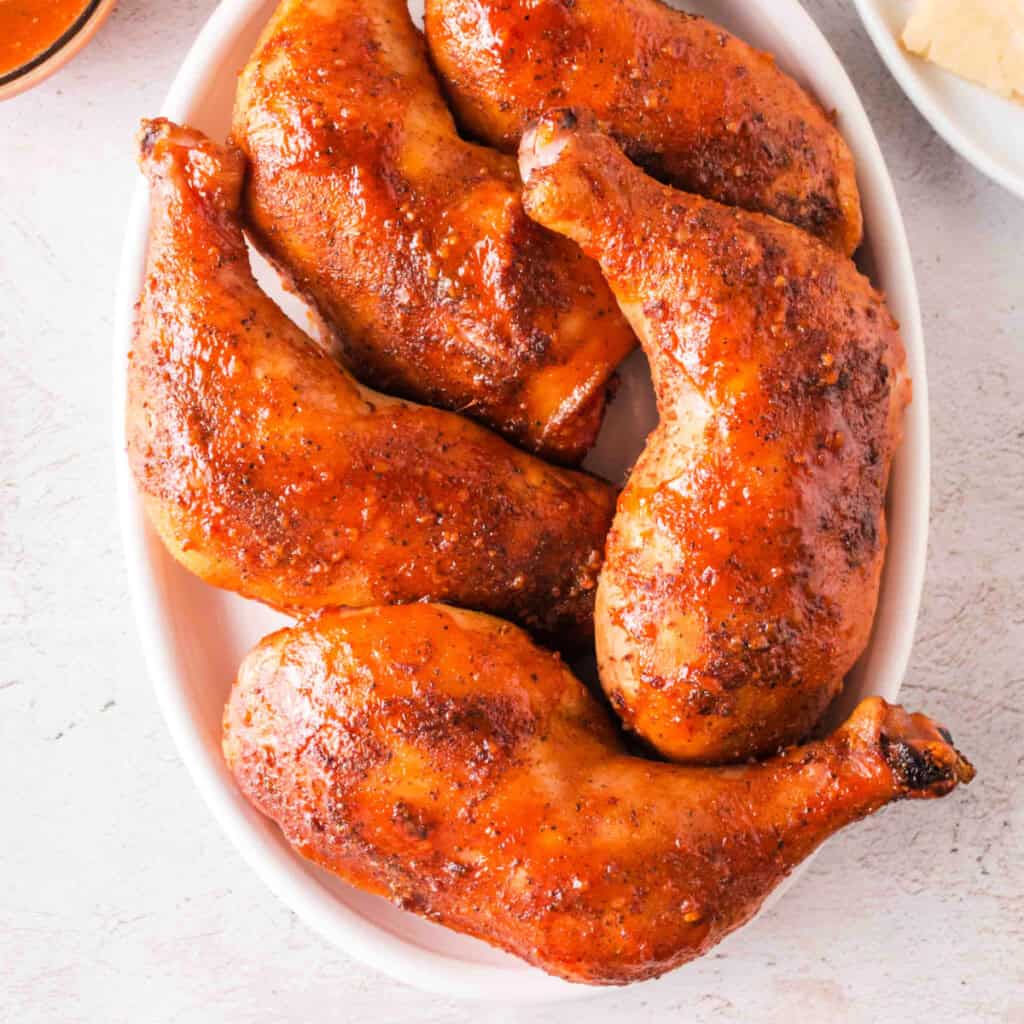 Top-down view of glazed smoked chicken leg quarters arranged in a dish