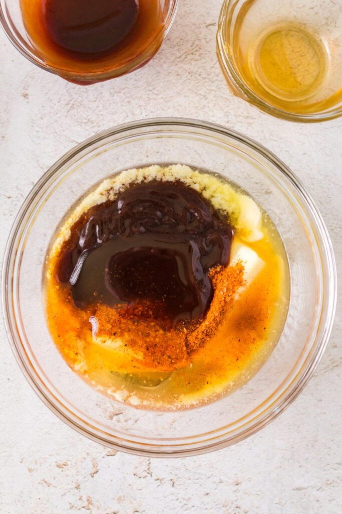 Ingredients for the BBQ sauce mixture in a glass bowl, including butter, BBQ sauce, and honey