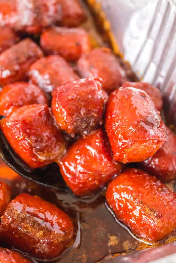 Close-up of cooked hot dog burnt ends with a glossy BBQ glaze in an aluminum tray