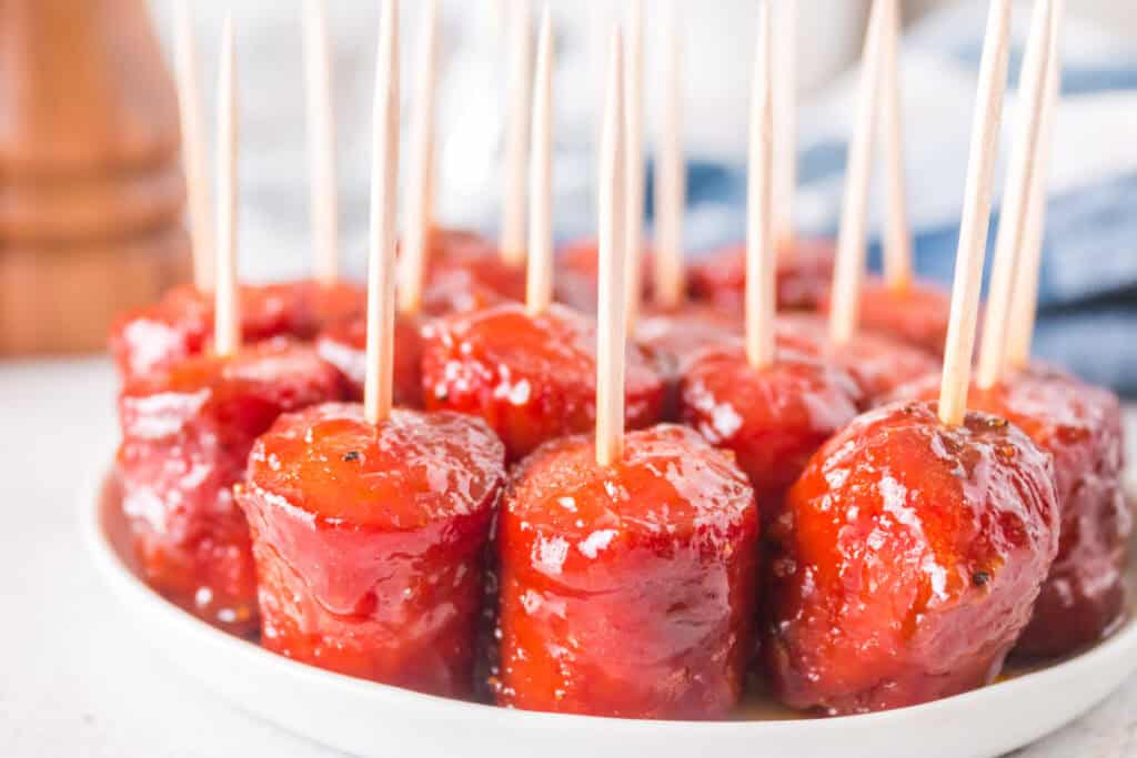 Glazed hot dog burnt ends served on a white plate with toothpicks for easy snacking