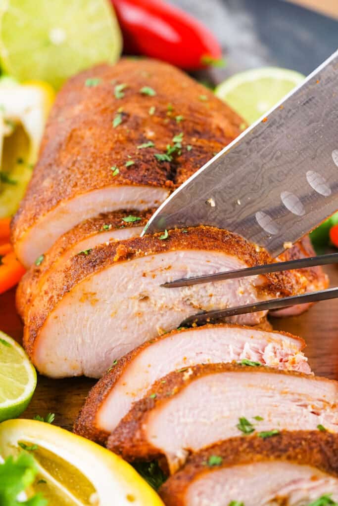 Juicy smoked turkey breast being sliced with a knife on a wooden cutting board