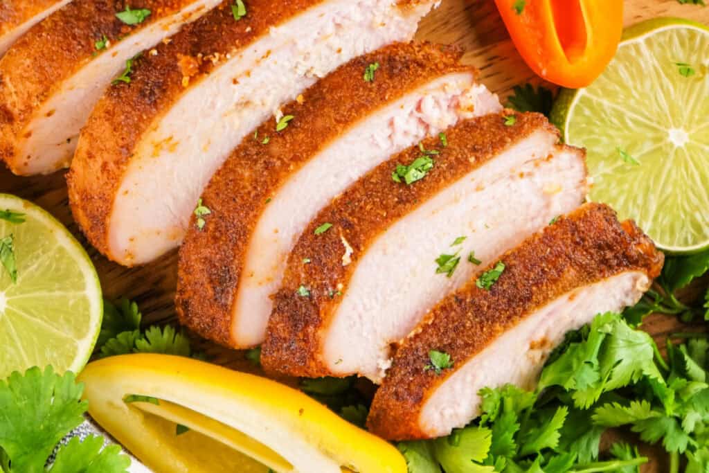 Sliced smoked turkey breast with a seasoned crust, lime wedges, cilantro, and peppers