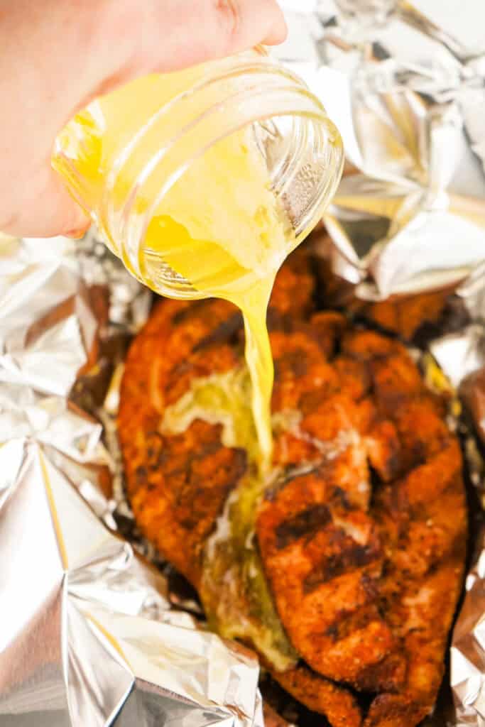 Melted butter being poured over seasoned smoked turkey breast in an aluminum foil wrap