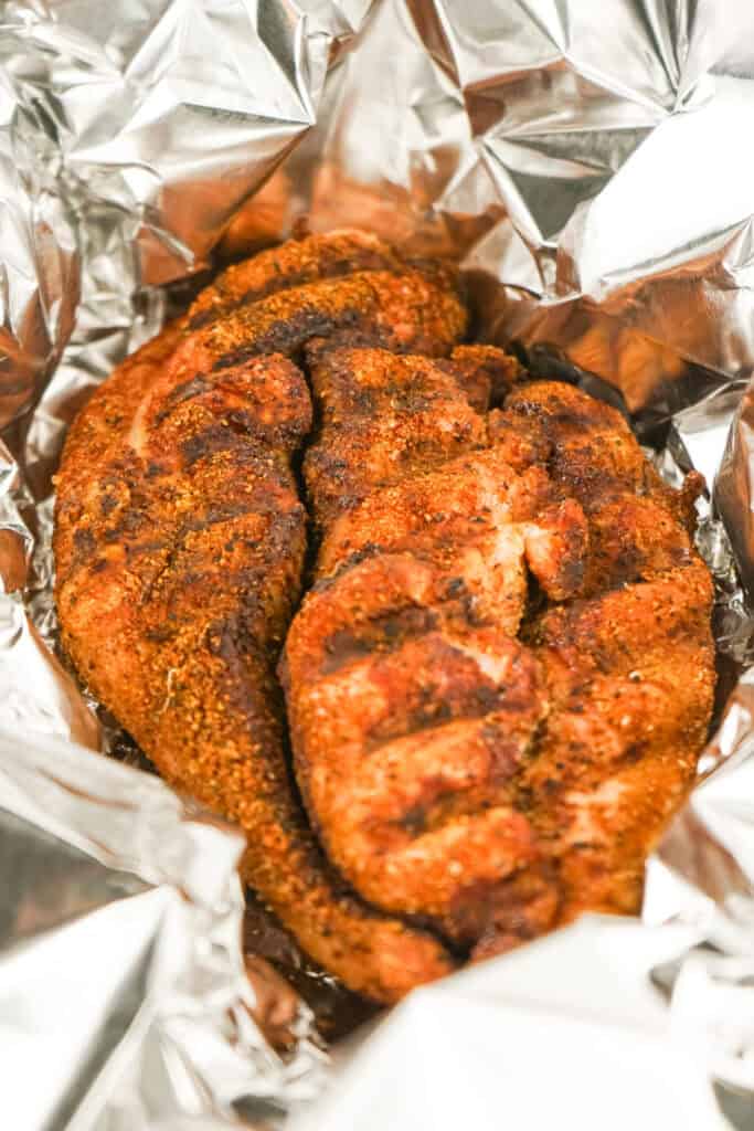 Seasoned smoked turkey breast resting inside an open aluminum foil wrap