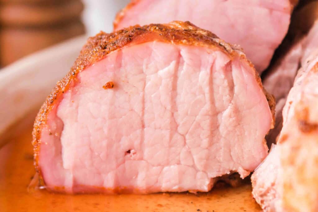 Close-up front view of sliced smoked pork tenderloin resting in pan juices