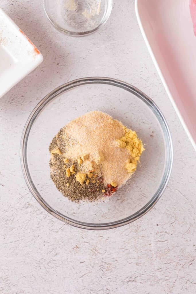 Close-up of seasoning mix in a glass bowl showing layers of spices before mixing