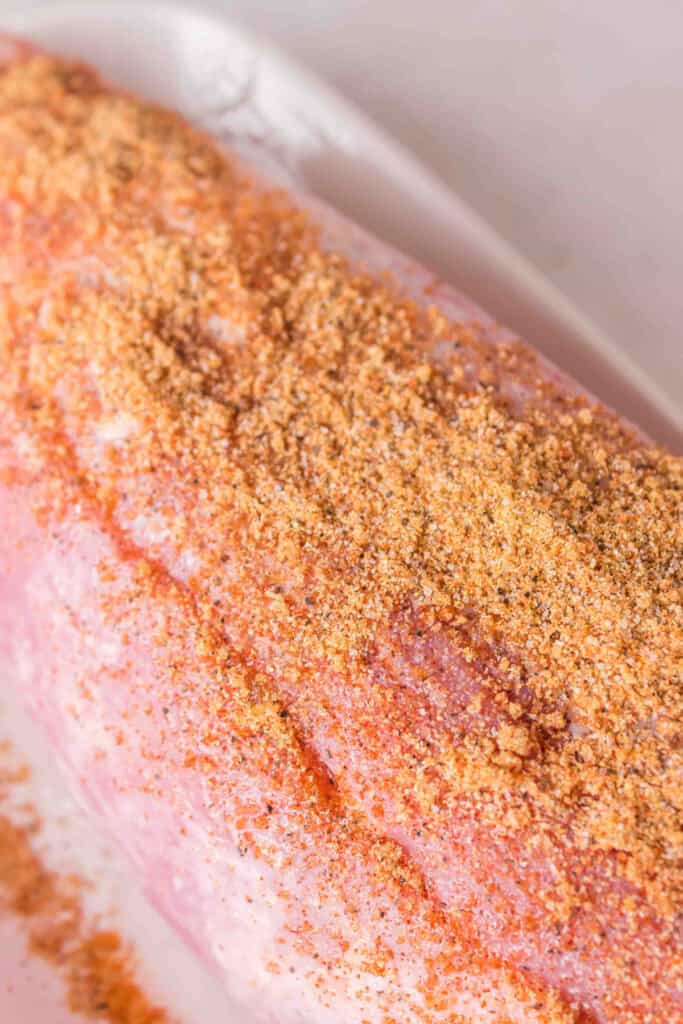 Pork tenderloin coated with dry rub seasoning on a white tray