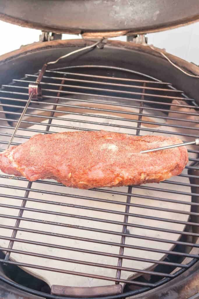 Pork tenderloin placed on a smoker grill with meat thermometer inserted