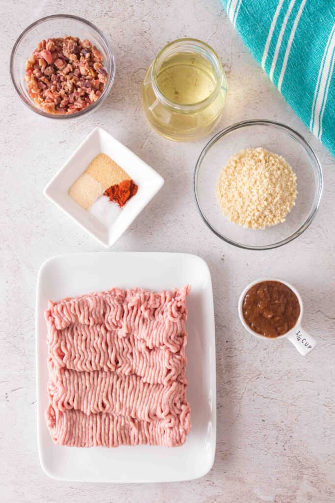 Overhead view of ingredients including ground turkey, bacon bits, seasonings, panko breadcrumbs, oil, and BBQ sauce.