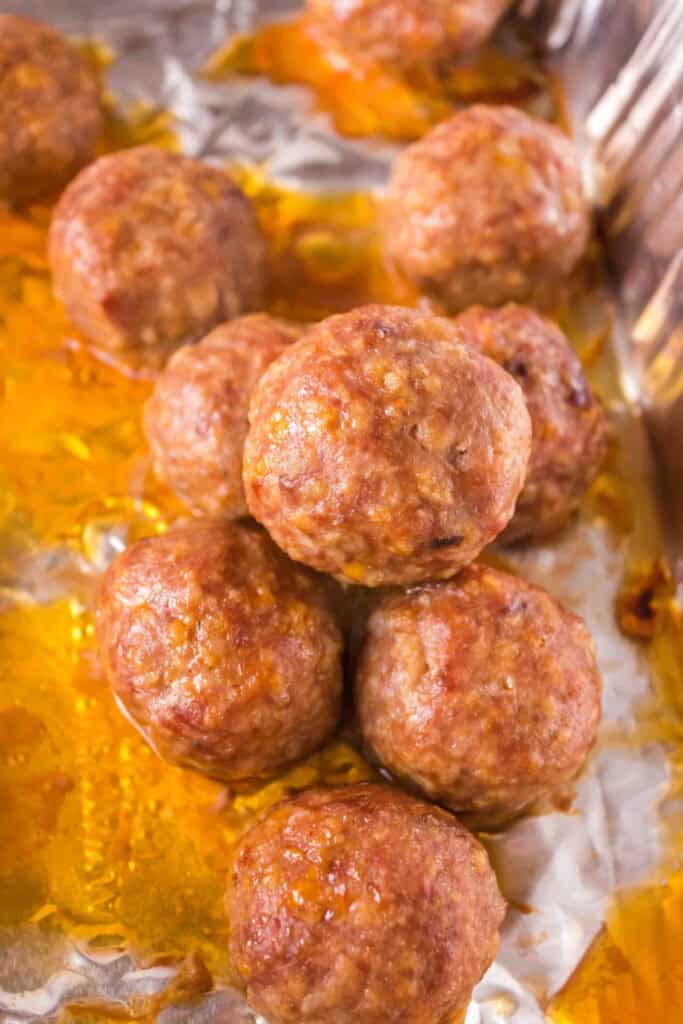 Cooked meatballs in a foil pan, surrounded by rendered juices.