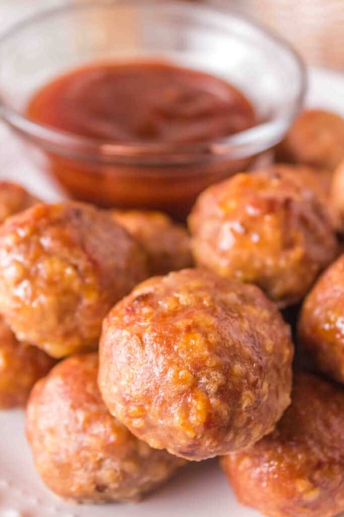 Close-up of smoked turkey meatballs piled on a plate with BBQ sauce in a glass bowl.