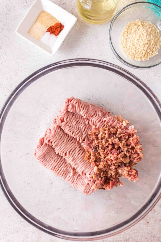 Ground turkey and bacon bits added to a large glass mixing bowl.