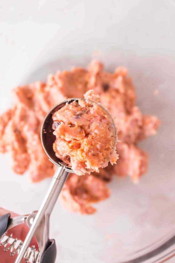A cookie scoop filled with raw turkey meatball mixture held over the bowl.