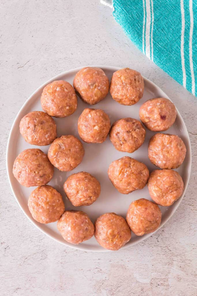 Raw turkey meatballs arranged neatly on a white plate, ready to cook.