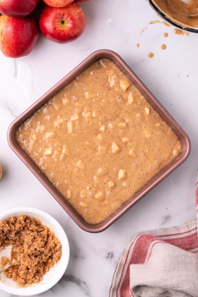Apple spice cake batter spread in a square pan before adding cinnamon topping