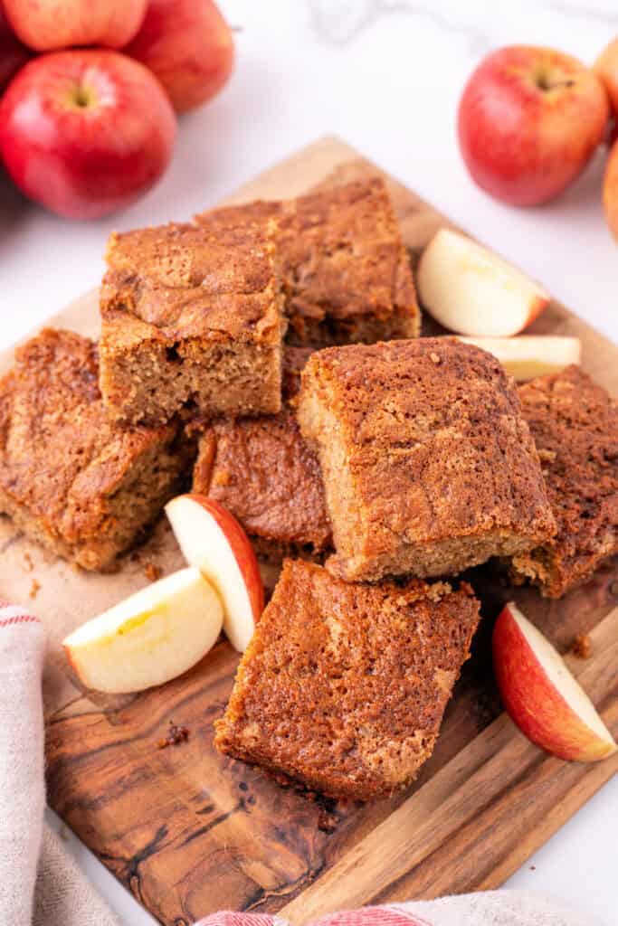 Pile of apple spice snack cake squares on a wooden board with apple slices
