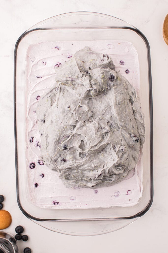 Blueberry pudding layer being added on top of the cheesecake layer
