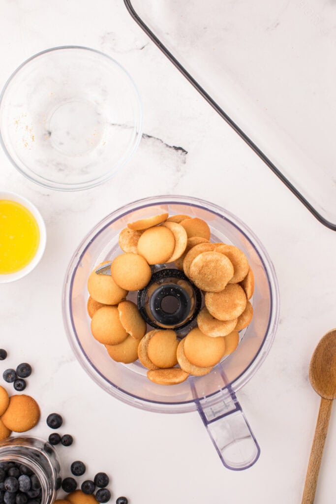 Vanilla sandwich cookies in a food processor with a glass baking dish nearby