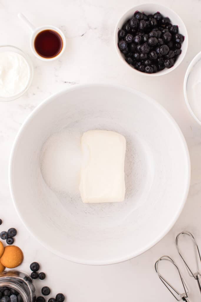Cream cheese and sugar in a large white mixing bowl ready to be beaten