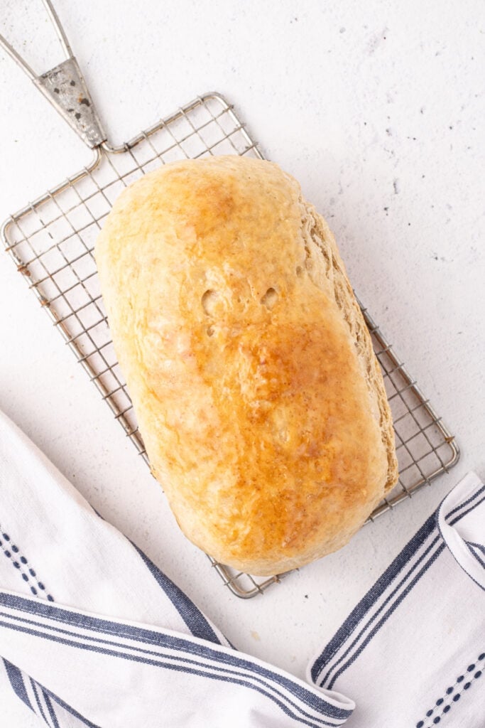 Freshly baked loaf of homemade bread cooling on a wire rack with a tea towel nearby