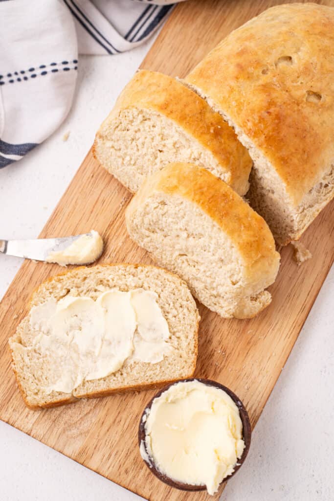 Sliced homemade bread with butter on a wooden cutting board and butter knife