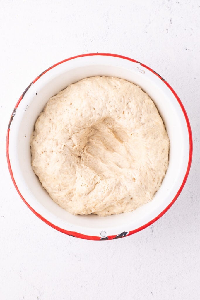 Dough risen and doubled in size in a white bowl with a hand mark showing it being punched down