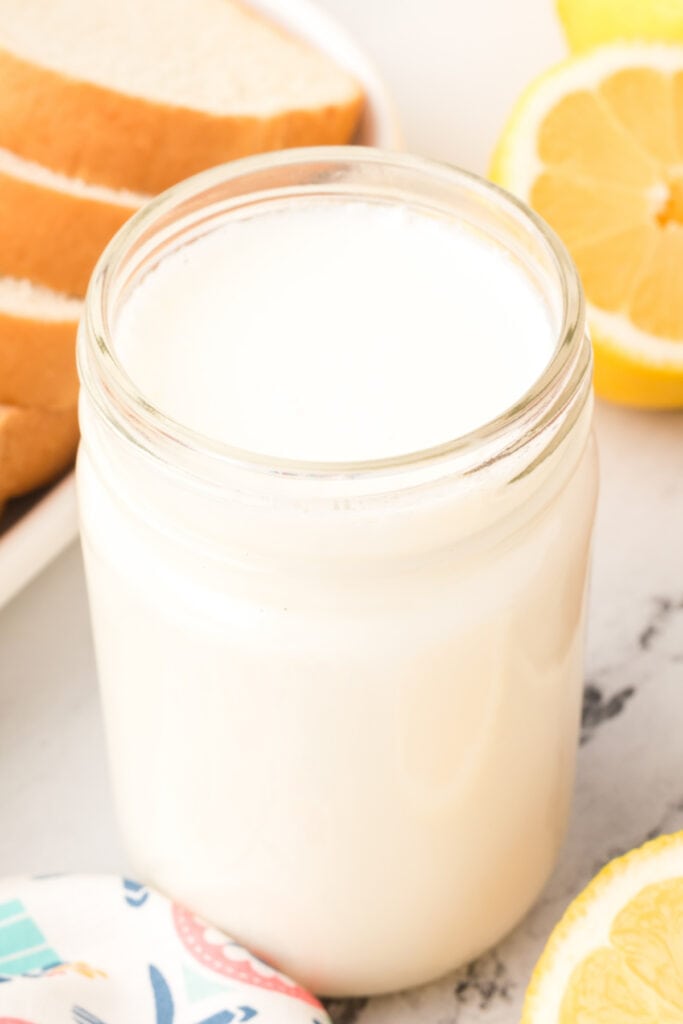 Close-up of a mason jar filled with buttermilk substitute beside lemons.