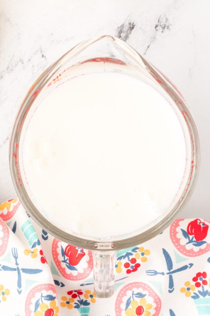 Overhead of milk added to the lemon juice and creating a thickened buttermilk substitute in a glass measuring cup.
