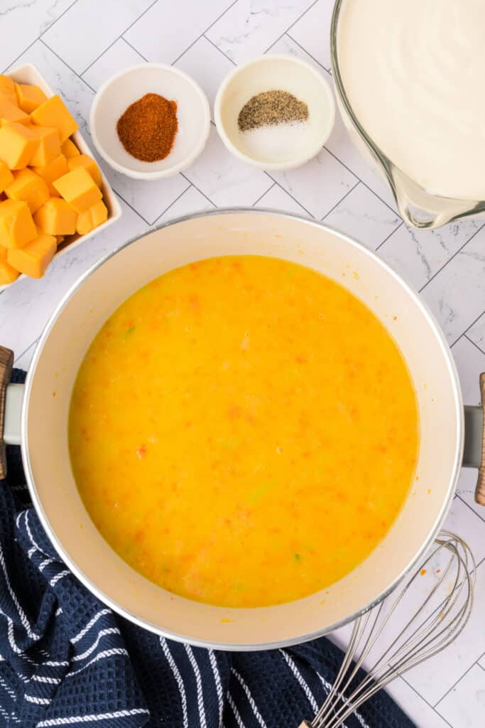Broth added and blended into the vegetable roux, forming a golden soup base. Whisk rests on the side.