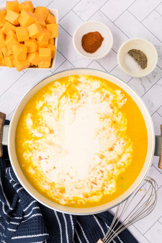 Heavy cream swirled into the vegetable and broth mixture in the pot before stirring.
